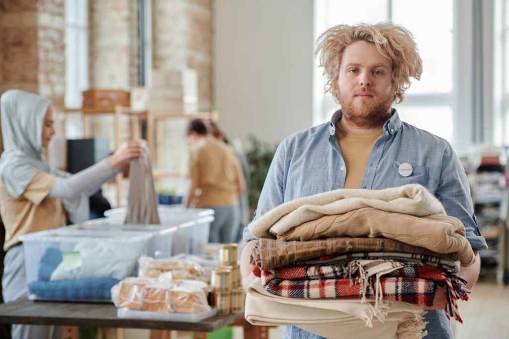 The Art of Drawing Readers In: Your attractive post title goes here A bearded man volunteers indoors, holding donated clothes for charity work amid a collaborative environment.